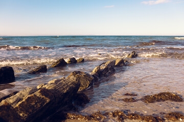 Beautiful sharp stones on the seashore, washed by the waves. Stone ridges on a wild beach. Smooth and long stone formations going into the sea. Beautiful photo of marine nature