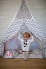 Adorable beautiful happy smiling ginger-haired toddler little girl is playing with her toys sitting in a teepee wigwam © Tina