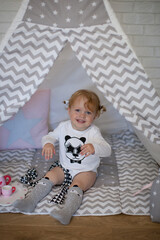 Adorable beautiful happy smiling ginger-haired toddler little girl is playing with her toys sitting in a teepee wigwam © Tina