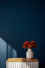 Minimalist interior with a white vase and red flowers on a ribbed bedside table against a deep blue wall © photoguns