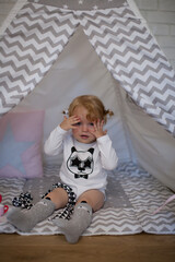 Adorable beautiful happy smiling ginger-haired toddler little girl is playing peekaboo sitting in a teepee wigwam © Tina