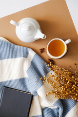 Cozy tea time setup with a white teapot, cup of tea, black book, and striped sweater on a dual-tone background. Perfect for autumn vibes and home comfort