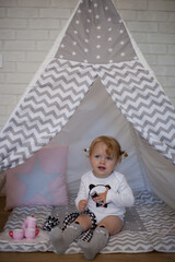 Adorable beautiful happy smiling ginger-haired toddler little girl is playing with her toys sitting in a teepee wigwam © Tina