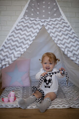 Adorable beautiful happy smiling ginger-haired toddler little girl is playing with her toys sitting in a teepee wigwam © Tina