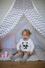 Adorable beautiful happy smiling ginger-haired toddler little girl is playing with her toys sitting in a teepee wigwam © Tina