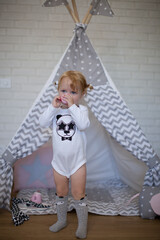 Adorable beautiful happy smiling ginger-haired toddler little girl is playing with her toys and drinking tea standing at the teepee wigwam © Tina