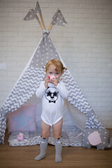 Adorable beautiful happy smiling ginger-haired toddler little girl is playing with her toys and drinking tea standing at the teepee wigwam © Tina