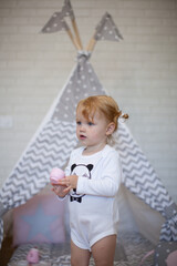 Adorable beautiful happy smiling ginger-haired toddler little girl is playing with her toys and drinking tea standing at the teepee wigwam © Tina