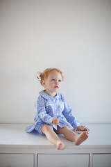 Aesthetic minimalistic portrait of Adorable beautiful smiling happy ginger-haired toddler baby girl sits on a white chest of drawers and plays with a toy horse