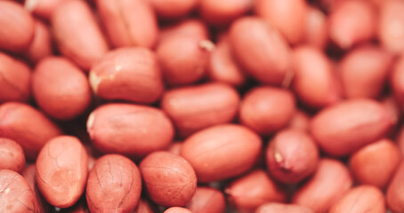 A bunch of peanuts are shown in a close up. The peanuts are all different sizes and are scattered...