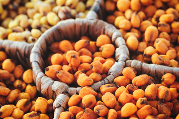 A wooden tray with a variety of nuts and seeds. The tray is filled with different colored nuts and seeds, including green, brown, and white. The nuts and seeds are scattered throughout the tray
