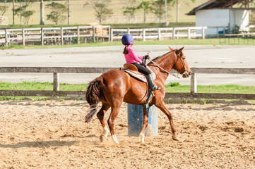 Model riding a horse practicing barrel racing on a farm with sand yard area