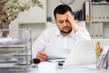 Obraz premium Exhausted male office worker sitting at desk. Tired man accountant doing his job.
