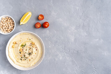Hummus with olive oil in a gray ceramic plate. Toast and breadsticks for snacks. Top view, on a gray background.