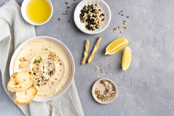 Hummus with olive oil in a gray ceramic plate. Toast and breadsticks for snacks. Top view, on a gray background.