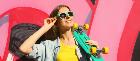 Stylish happy young girl with skateboard in glasses, modern teenager posing against on graffiti wall