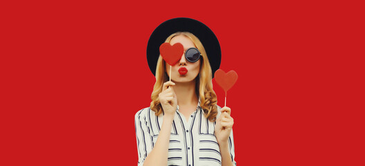 Portrait of beautiful young woman blowing her lips sends kiss with sweet red heart shaped lollipop