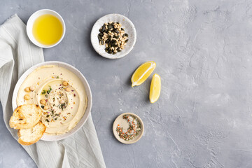 Hummus with olive oil in a gray ceramic plate. Toast and breadsticks for snacks. Top view, on a gray background.