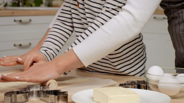 A child and an adult roll out dough together, preparing for baking in a bright kitchen filled with baking tools and ingredients.