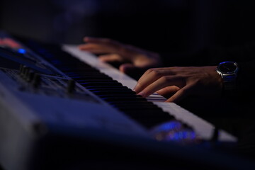 A striking close-up of a Black man's hands gracefully dancing over a keyboard, illuminated by cinematic lighting. The dark, moody atmosphere, combined with backlighting and a blurred background, creat