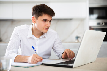 Fototapeta premium concentrated young man working on laptop and making notes in notebook
