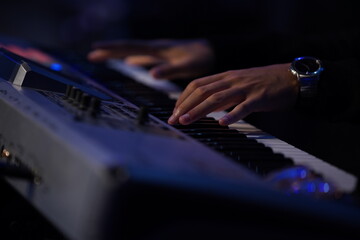 A striking close-up of a Black man's hands gracefully dancing over a keyboard, illuminated by cinematic lighting. The dark, moody atmosphere, combined with backlighting and a blurred background, creat
