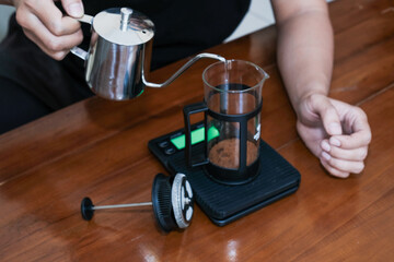 Closeup a hand Pouring the hot water into coffee powder on the french press glass, Brewing method French press coffee maker.