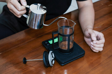 Closeup a hand Pouring the hot water into coffee powder on the french press glass, Brewing method French press coffee maker.