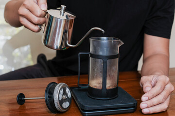 Closeup a hand Pouring the hot water into coffee powder on the french press glass, Brewing method French press coffee maker.