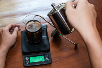 Closeup a hand Pouring the hot water into coffee powder on the french press glass, Brewing method French press coffee maker.