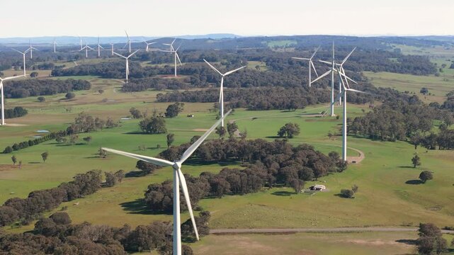 Aerial drone pullback reverse view of an array of large wind turbines at Biala and Gullen Range Wind Farm, Bannister in the Southern Tablelands region of New South Wales, Australia on a sunny day 