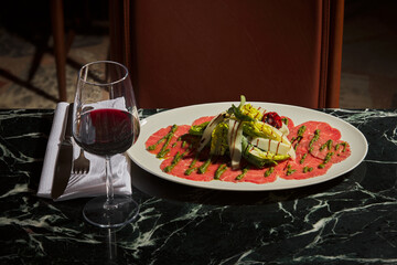 Beef Carpaccio and red wine. Served with arugula, parmesan, homemade pesto, white truffle sauce, lactose, pistachios, mustard and wine. Luxurious and expensive gourmet meal on a black marble table.