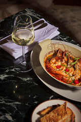 Oven-baked jumbo shrimps and a glass of white wine. Luxurious and expensive gourmet meal prepared on a black marble table, served with a glass of wine. Large shrimps cooked in tomato sauce. Close-up
