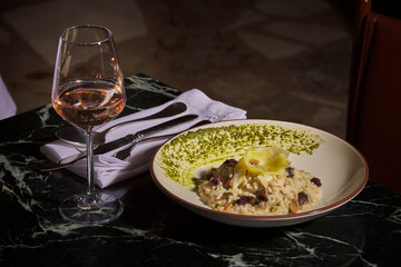 Mushroom risotto with pink wine. Luxurious and expensive gourmet meal prepared on a black marble table, served with a glass of wine