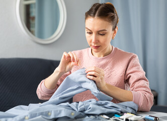 Woman sewing button on a shirt sleeve at home