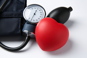Blood pressure measuring device and red decorative heart on light background, closeup