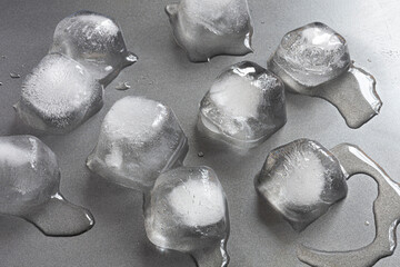 A top view image of several large ice cubes melting on a grey metal background.