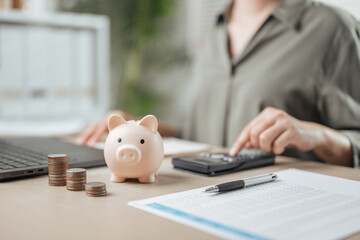 finance, wealth, income, growth, piggybank, expense, insurance, retirement, invest, invoice. A woman is sitting with a piggy bank, calculator, and a stack of coins. She is working on a budget.