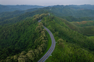 Fototapeta premium Aerial view of countryside winding road passing through the green forest and mountain in Thailand.