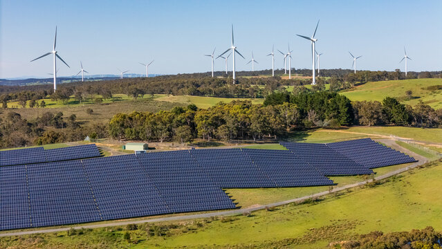 Aerial drone view of a hybrid solar and wind farm showing the large wind turbines in the background for renewable clean energy supply located at Bannister, NSW, Australia on a sunny day