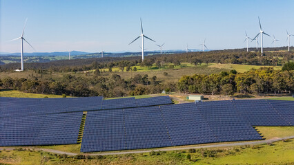 Aerial drone view of a hybrid solar and wind farm showing the large wind turbines in the background...