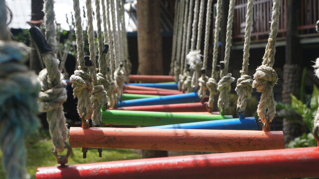 Perspective view of a colorful rope bridge with red, green, and blue wooden planks suspended by sturdy ropes