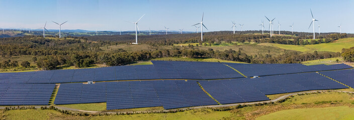 Panoramic aerial drone view of a hybrid solar and wind farm showing the large wind turbines in the...