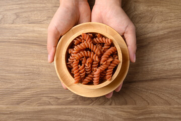 Raw orange fusilli pasta in bowl holding by hand on wooden background, Food ingredient, Table top view