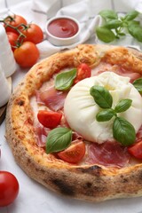 Delicious pizza with burrata cheese, basil, tomatoes and ham on table, closeup