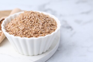 Buckwheat bran in bowl on white marble table, closeup. Space for text