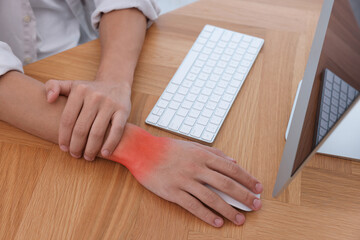 Man suffering from pain in wrist while using computer mouse at wooden table, closeup. Office work,...