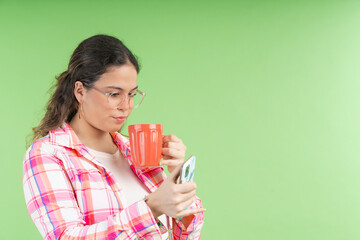 Young woman drinking coffee and browsing on smartphone on green background