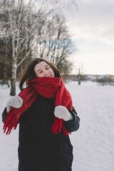 A smiling woman with a red scarf enjoys a snowy winter day in a serene forest setting beneath a...