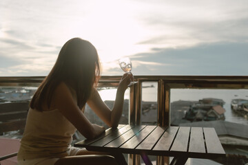 Single woman having a drink alone, enjoy the asian sea village view sunset.